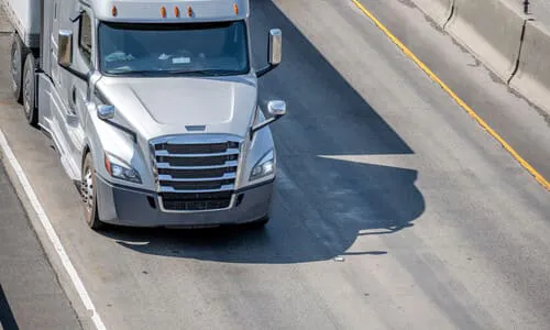 A large, silver truck pulling a trailer behind it along a highway.