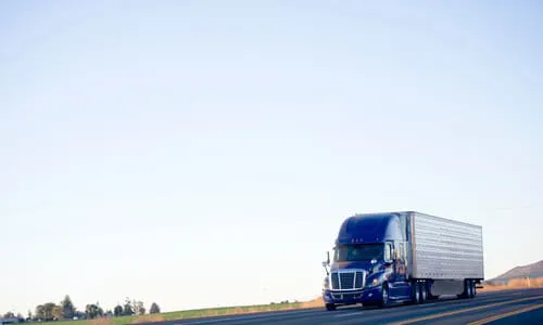 A blue semi trailer truck driving on an open road and transporting cargo.