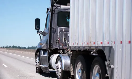 A grey big rig truck pulling a trailer on a California highway.
