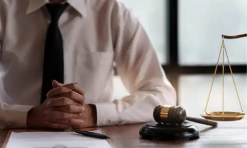 A personal injury lawyer clasping his hands at his desk next to scales and a gavel.