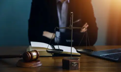 A personal injury lawyer with crossed arms seated behind his desk with an open law book, a gavel, and scales.