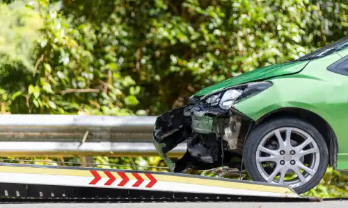 A green vehicle going up a ramp of a tow truck to get repairs after an accident.