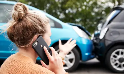 A woman calling for legal assistance on her phone after a car accident with another vehicle.