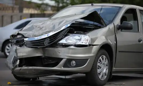 A grey car whose hood was crumpled in an accident on a city road.