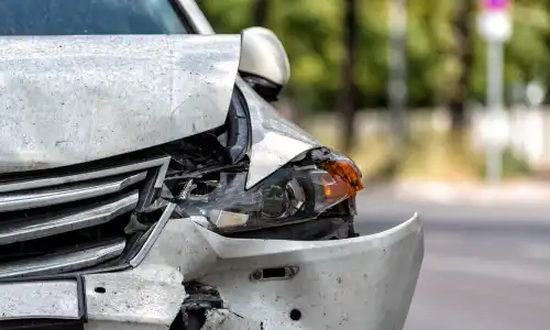 The driver-side headlight of a grey family sedan damaged in an accident.