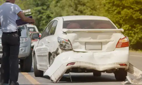 An accident victim going through his insurance policy while standing next to his damaged vehicle.