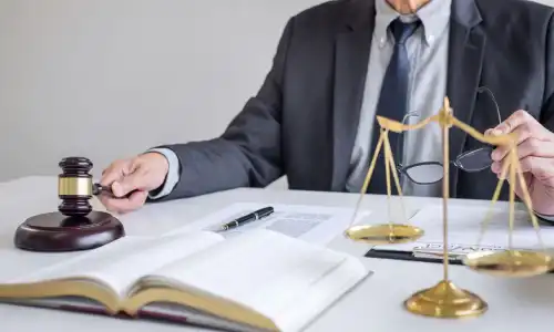 A personal injury lawyer holding a gavel in one hand and a pair of glasses in the other while working on a case.