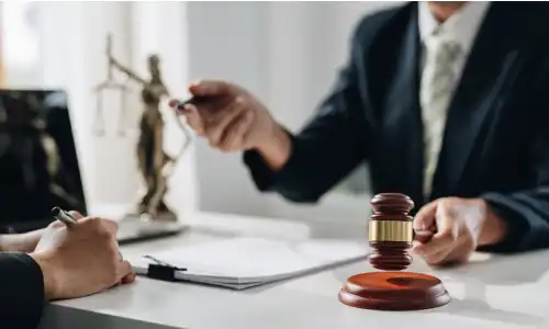 A personal injury lawyer in his office holding a gavel in one hand while explaining a client's rights to them.