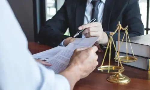 A lawyer sitting across his client and pointing at important details in a document using his pen.