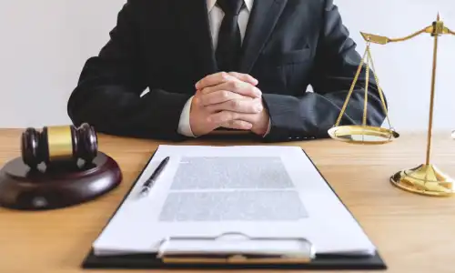 A personal injury lawyer clasping his hands with a client's insurance policy on a clipboard before him.