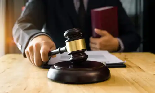 A personal injury lawyer with a law book under one arm, and holding a gavel over a soundblock with the other hand.