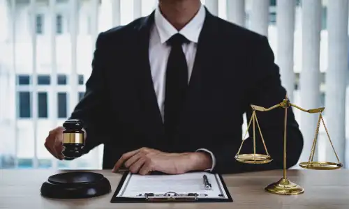 A lawyer holding up a gavel over a soundblock in one hand and resting the other arm on his desk.