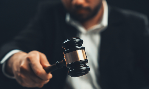 A lawyer in his office holding up a gavel over its soundblock from behind his desk.