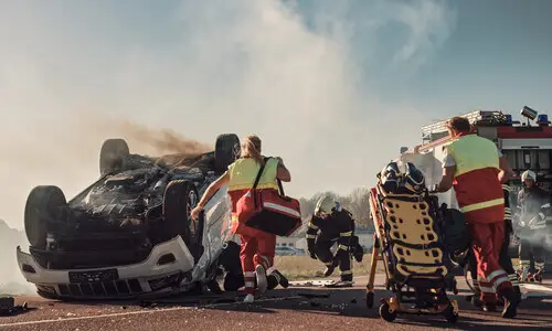 Car accident with rescue workers and fire department personnel rushing to the scene.