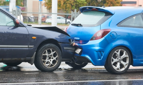 A dark sedan and bright blue hatchback involved in a rear-end accident.