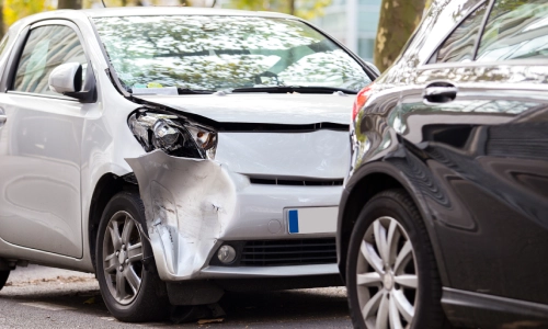 A rear-end collision between a white and a black car with the vehicles on the side of the road.